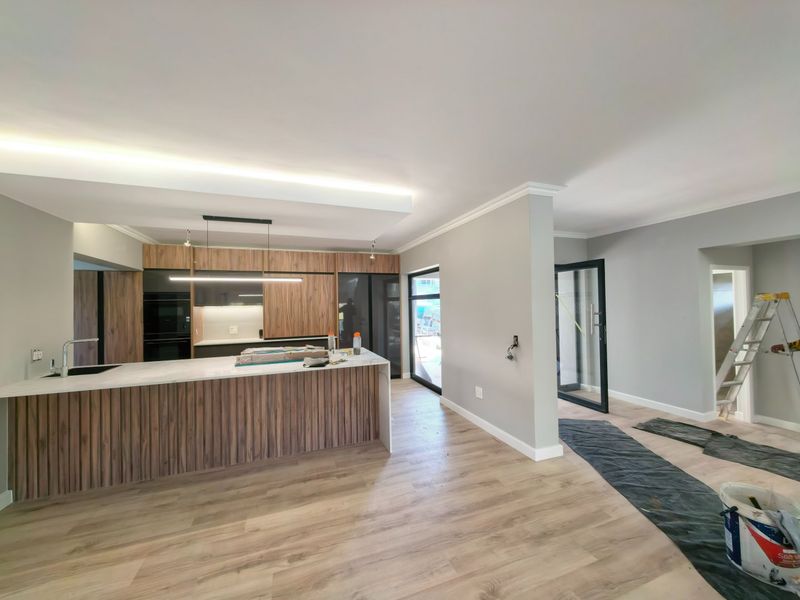 Modern open-plan kitchen featuring wood-grain cabinetry, a stone-topped island, and integrated appliances, currently in the final stages of construction.