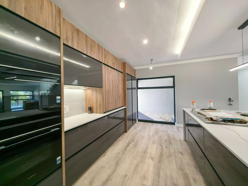 Modern kitchen featuring high-end cabinetry, integrated Siemens ovens, stone countertops, and sleek wood-look flooring with contemporary recessed and cove lighting.