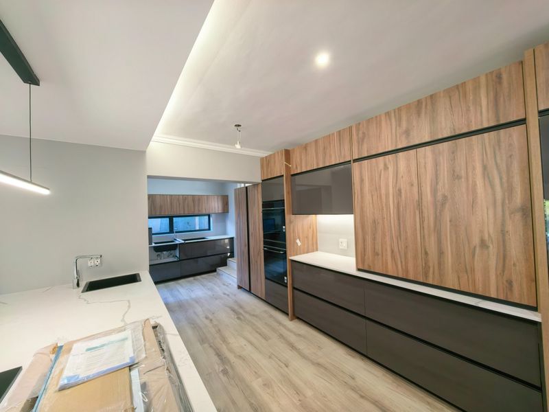 Modern kitchen featuring sleek wood-grain and dark cabinetry, stone countertops, integrated appliances, and recessed lighting in a clean, contemporary design.