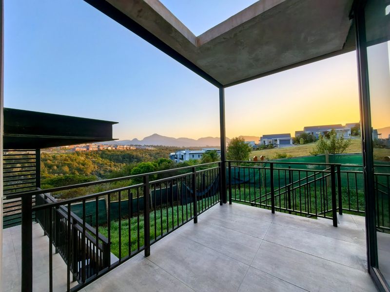 A modern covered balcony featuring tiled flooring, metal railings, and expansive views of the surrounding landscape and mountains.