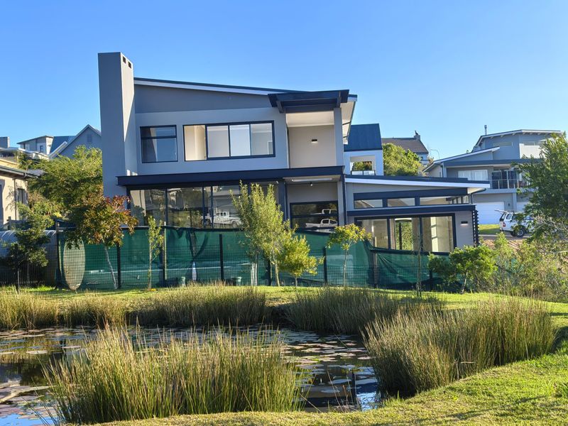 A modern double-story residence featuring large glass windows, a prominent chimney, and a covered patio overlooking a natural pond and landscaped garden.