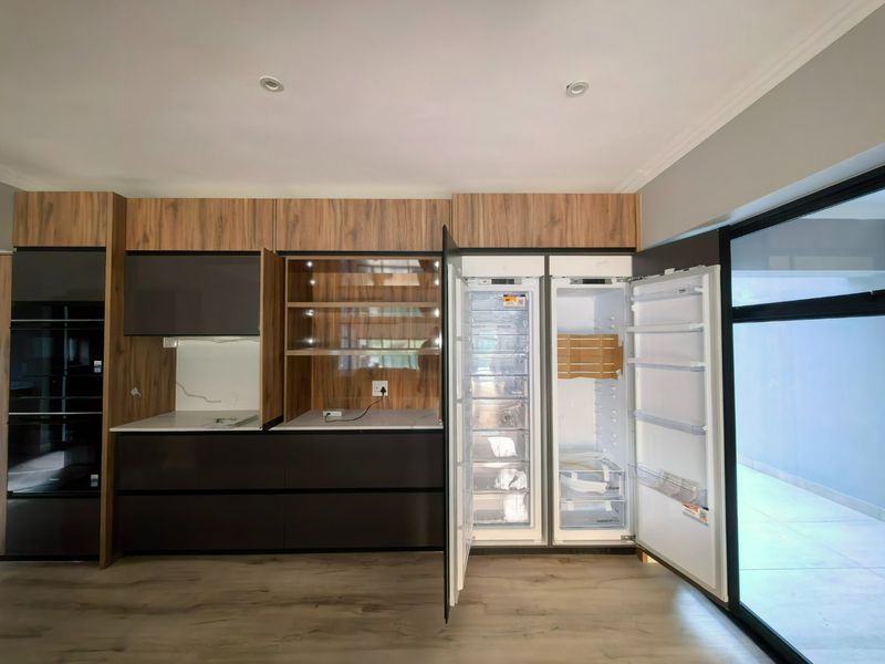 Modern kitchen featuring sleek wood-grain and dark cabinetry, integrated appliances, stone countertops, and direct access to an outdoor area through sliding glass doors.