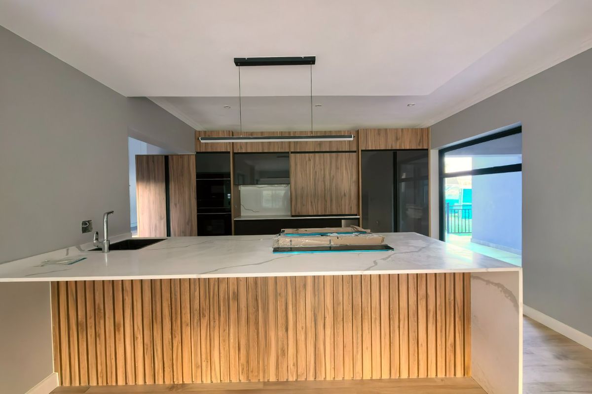 Modern kitchen featuring a large stone-topped island with wood-slat detailing, integrated cabinetry, and sleek pendant lighting in a contemporary open-plan space.