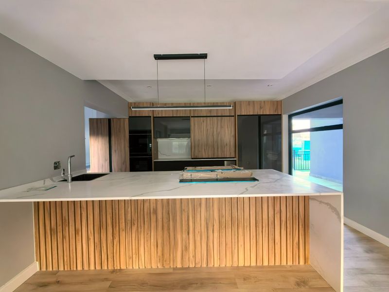 Modern kitchen featuring a large stone-topped island with wood-slat detailing, integrated cabinetry, and sleek pendant lighting in a contemporary open-plan space.
