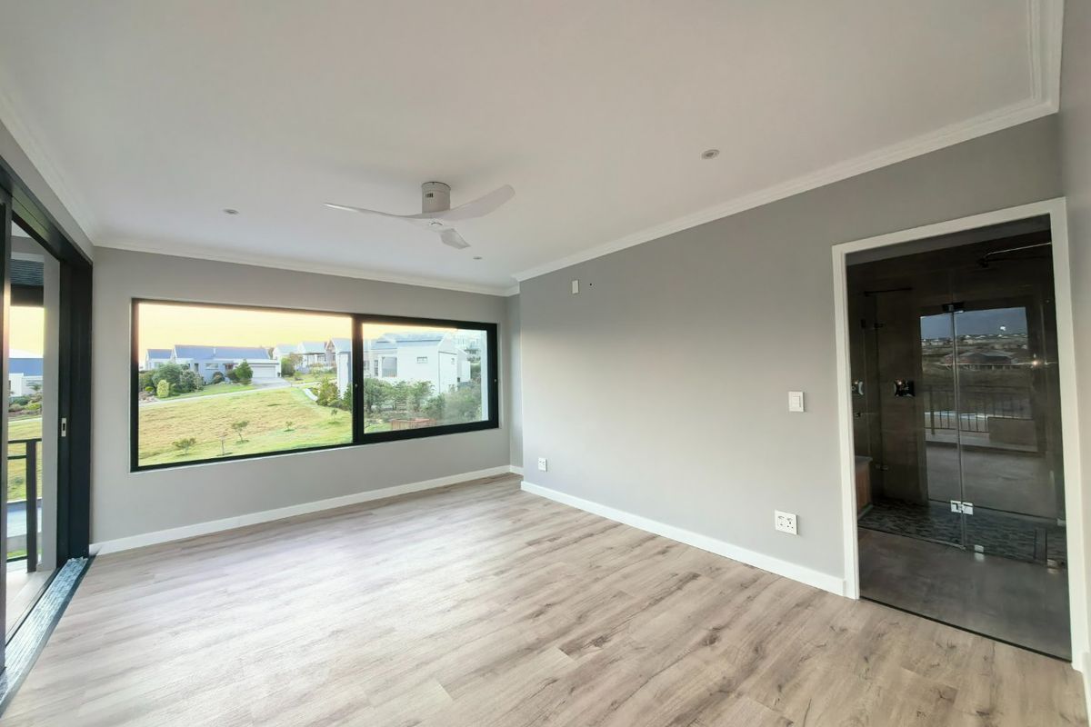 A bright, modern bedroom featuring laminate flooring, a ceiling fan, large windows with scenic views, and direct access to an en-suite bathroom.