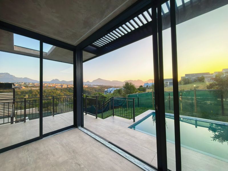 A modern, empty covered patio featuring large sliding glass doors, tiled flooring, and direct access to a swimming pool with scenic mountain views.