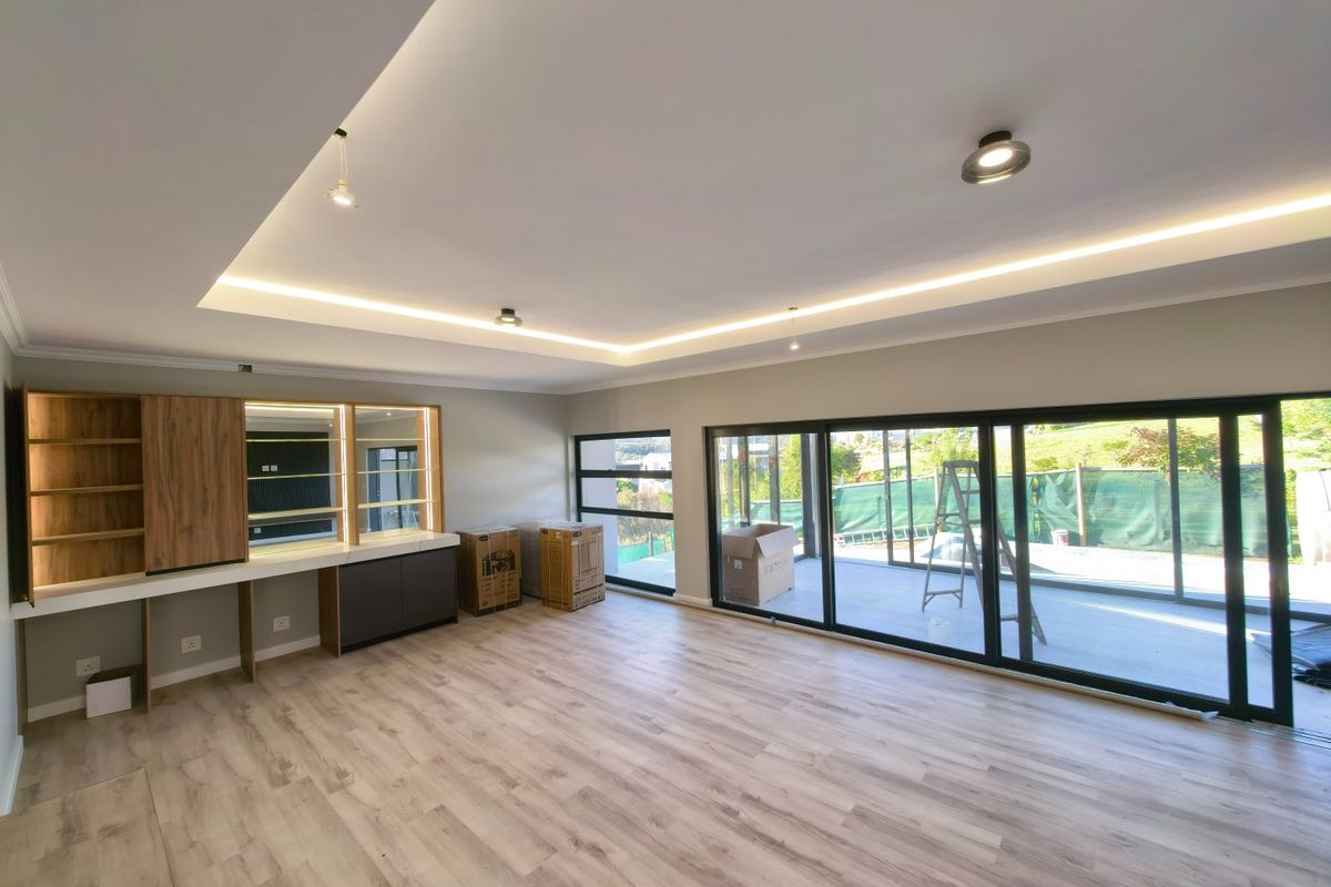 Spacious living area featuring modern recessed cove lighting, built-in cabinetry, and large sliding glass doors that open to an outdoor patio area.