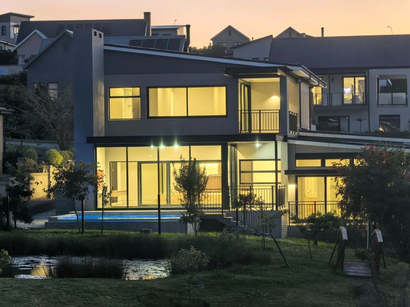 Modern double-story residence featuring expansive glass walls, a private swimming pool, and a balcony overlooking a landscaped garden at dusk.