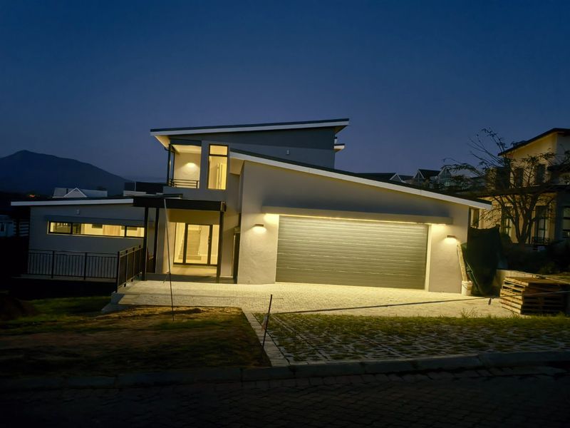 Modern double-story residential property featuring a paved driveway, integrated double garage, and contemporary architectural lighting at dusk.