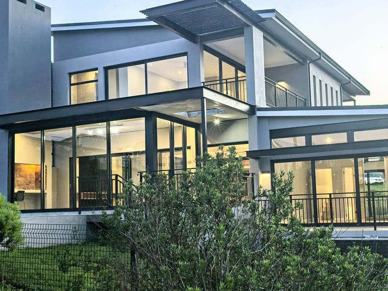A modern multi-level rear facade featuring extensive glass sliding doors, a balcony with metal railings, and a contemporary steel pergola structure.