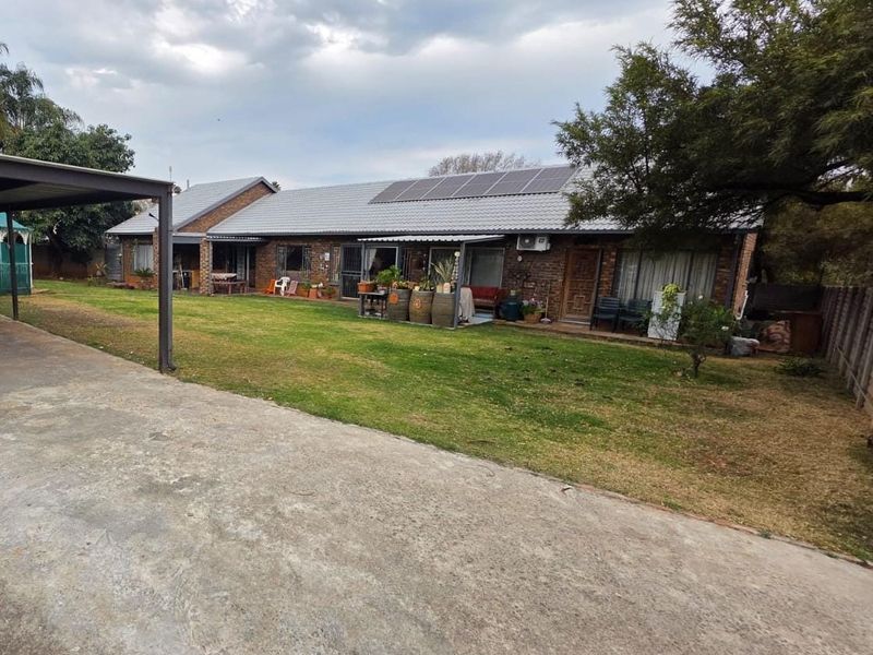 Rear view of the house featuring a brick facade, tiled roof with solar panels, a concrete driveway, and a covered patio area overlooking the garden.