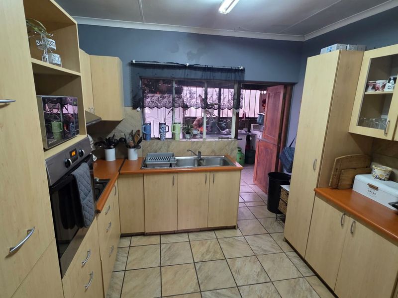 A functional kitchen featuring light wood cabinetry, laminate countertops, a stainless steel double sink, and tiled flooring with direct access to an adjacent utility area.