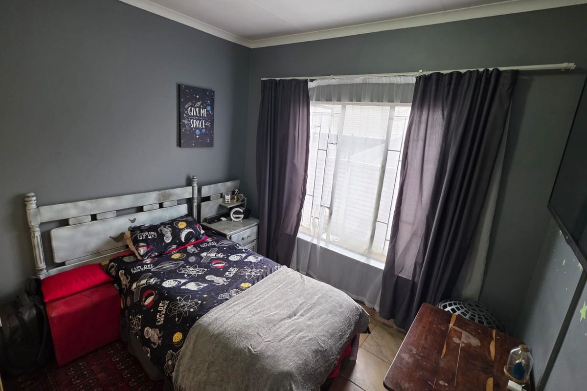 A bedroom featuring dark grey walls, tiled flooring, and a window with curtain rails, providing a functional space for rest.