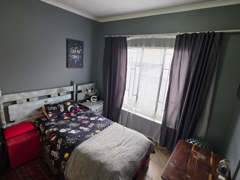 A bedroom featuring dark grey walls, tiled flooring, and a window with curtain rails, providing a functional space for rest.