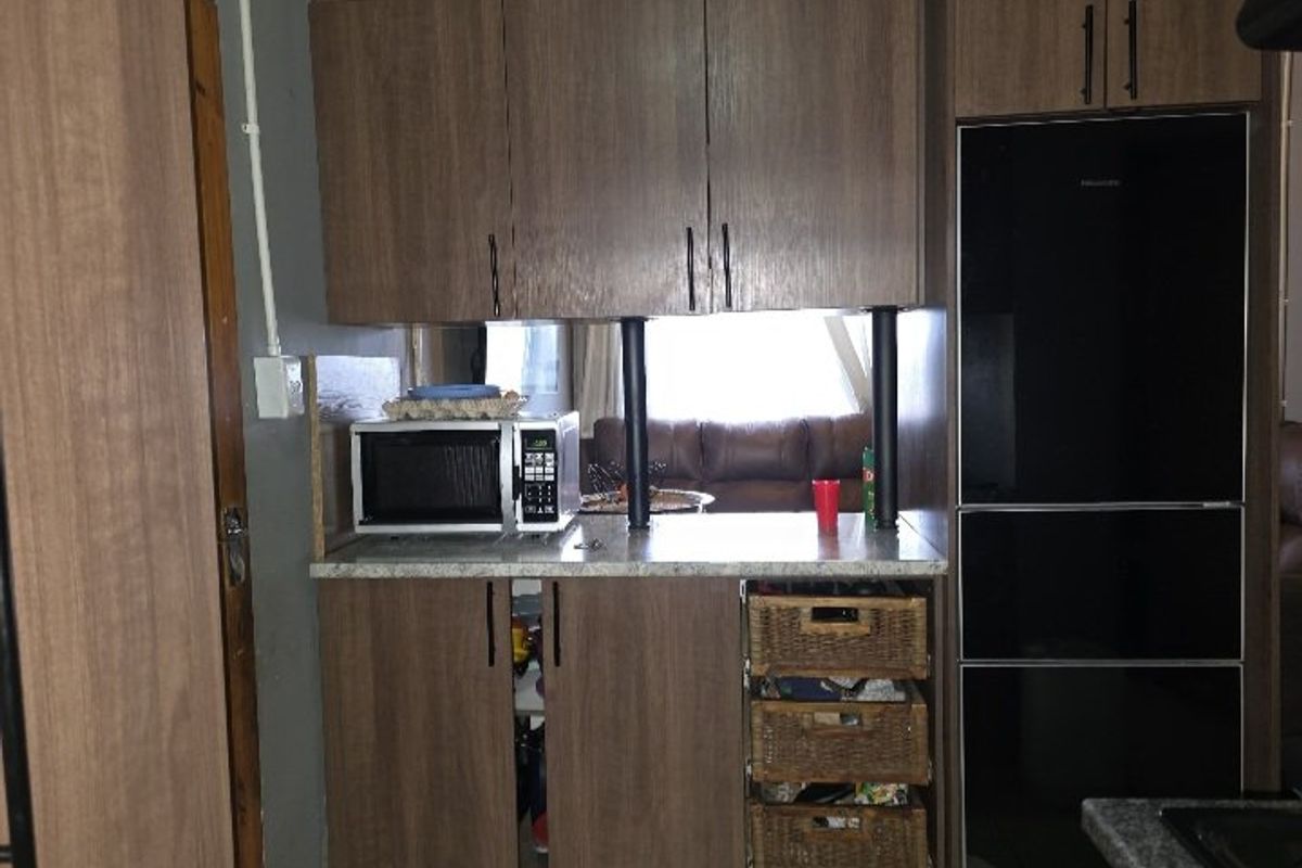A compact kitchen area featuring wood-look cabinetry, laminate countertops, and integrated appliances, with visible exposed electrical conduit and unfinished detailing.