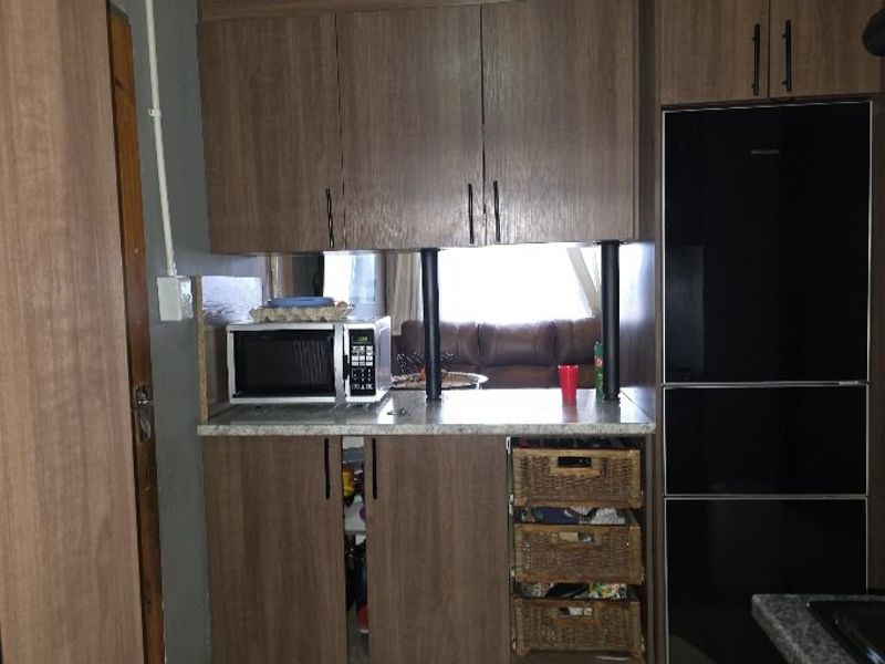 A compact kitchen area featuring wood-look cabinetry, laminate countertops, and integrated appliances, with visible exposed electrical conduit and unfinished detailing.