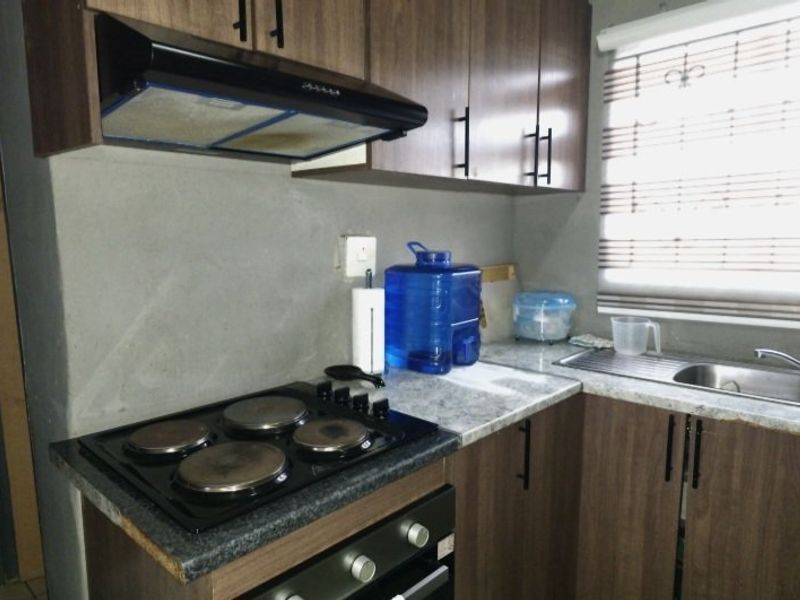 Compact kitchen featuring dark wood-look cabinetry, stone-effect countertops, built-in electric oven and hob, extractor fan, and a stainless steel sink.