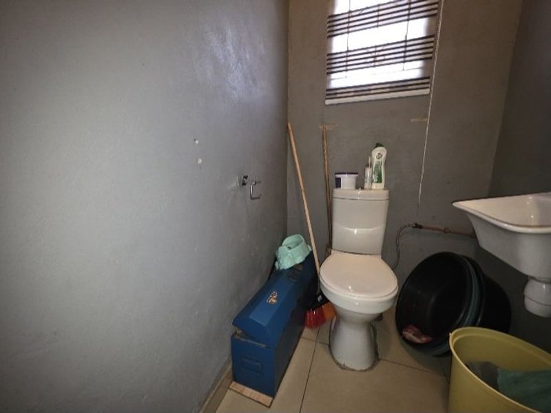 A small bathroom featuring a toilet and basin, currently requiring cosmetic updates and finishing to the wall surfaces and exposed plumbing.