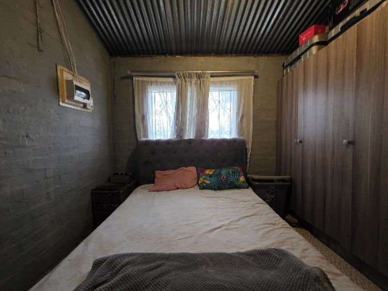 A bedroom featuring exposed brick walls, a corrugated metal ceiling, and a built-in wardrobe, requiring cosmetic updates to improve the overall finish.