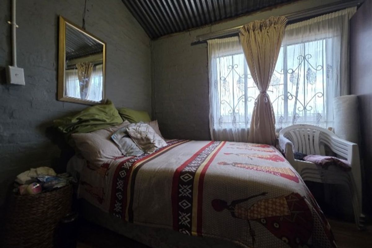 A bedroom featuring exposed brick walls and a corrugated iron roof, with security burglar bars on the window.