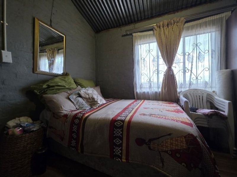 A bedroom featuring exposed brick walls and a corrugated iron roof, with security burglar bars on the window.
