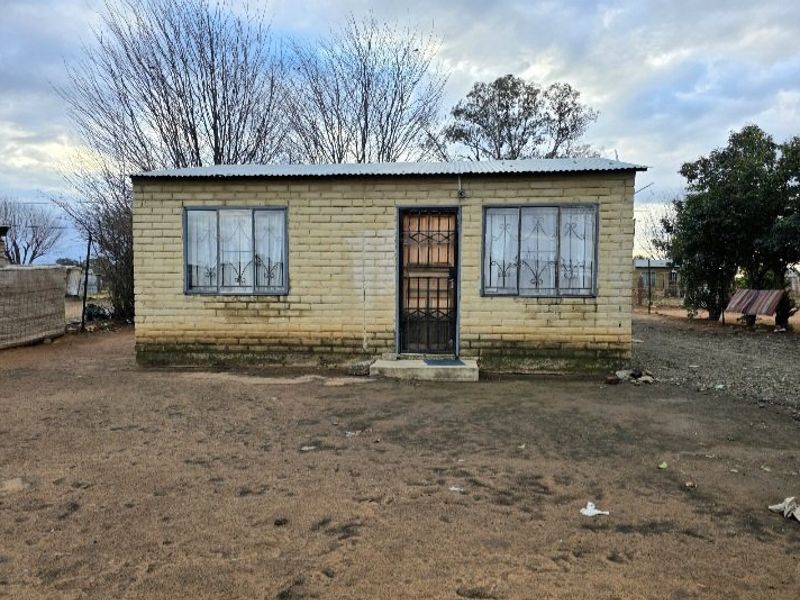 Front elevation of a single-story brick house featuring a corrugated metal roof, security gate, and window security bars.