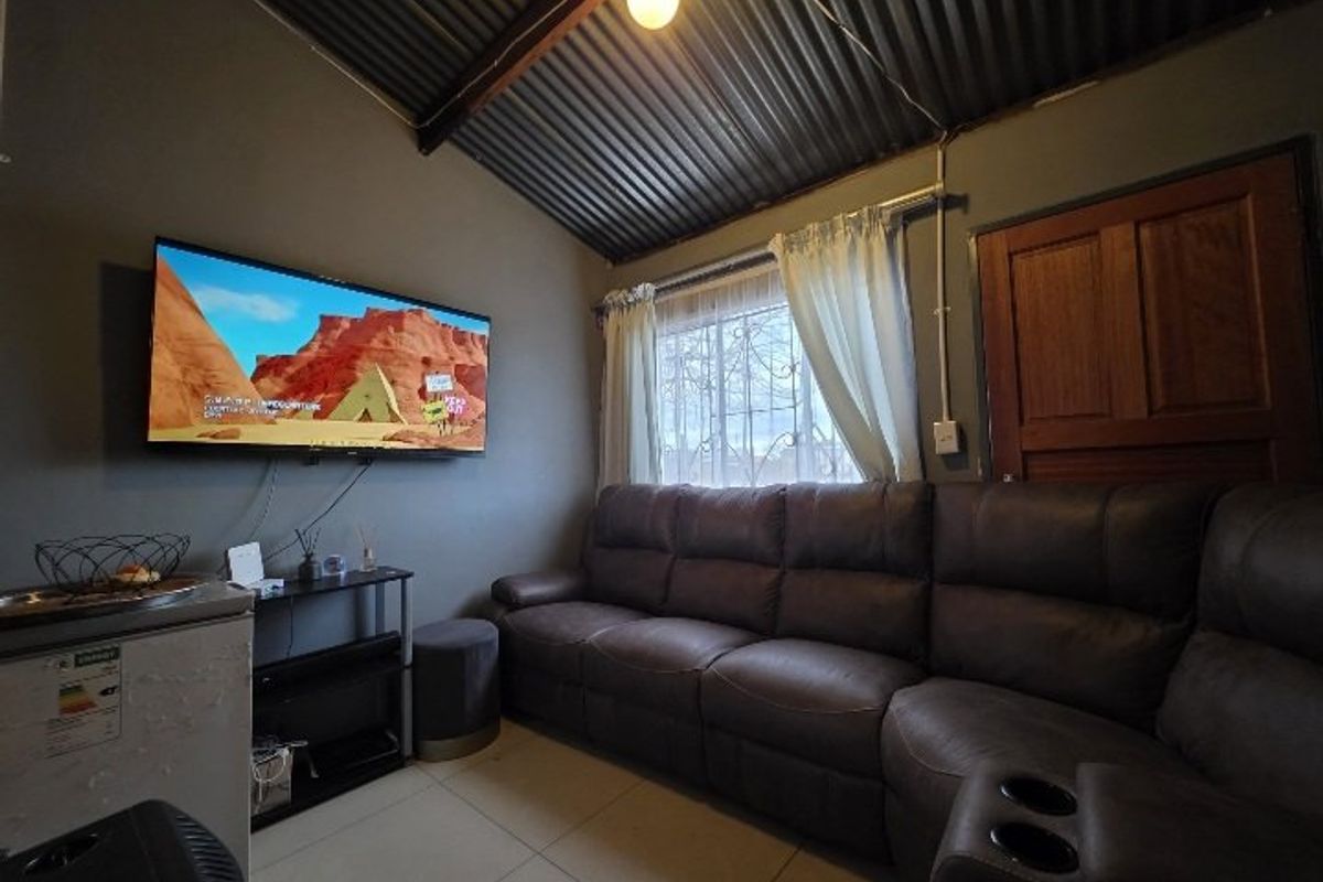 A compact living room featuring tiled floors, exposed timber rafters, and a corrugated iron ceiling, providing a rustic aesthetic.