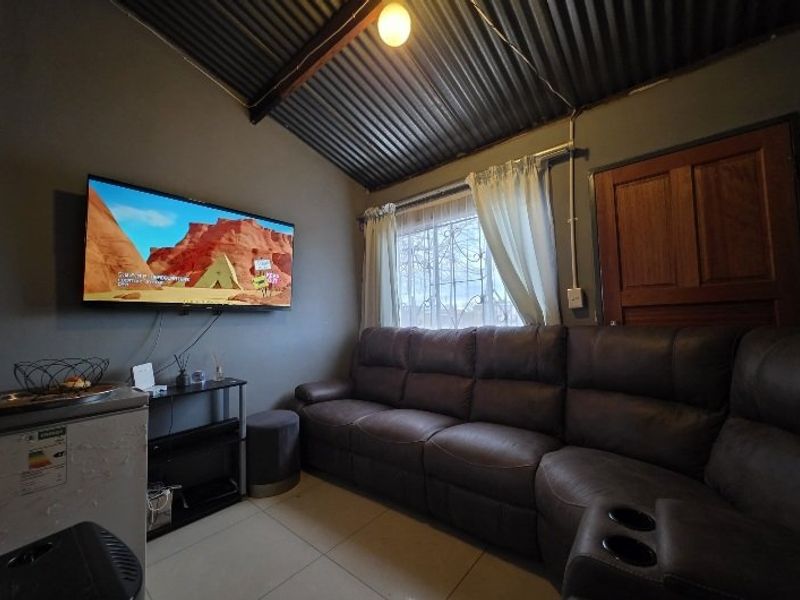 A compact living room featuring tiled floors, exposed timber rafters, and a corrugated iron ceiling, providing a rustic aesthetic.