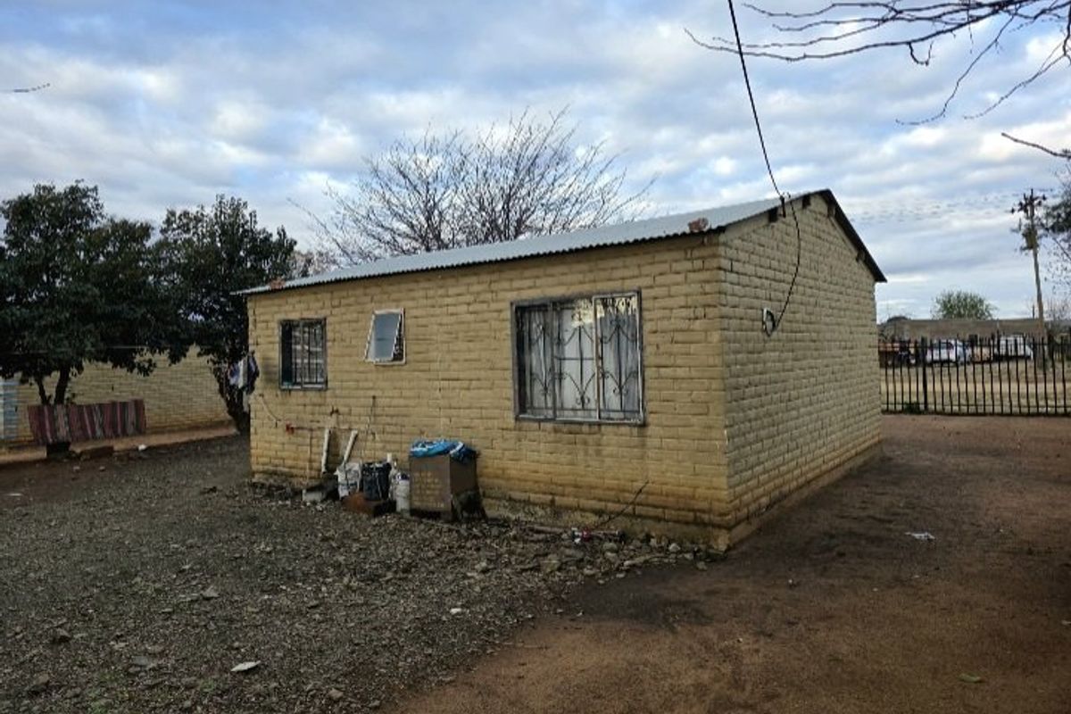 A detached single-story brick structure featuring a corrugated metal roof and security-barred windows, situated on an unpaved lot.