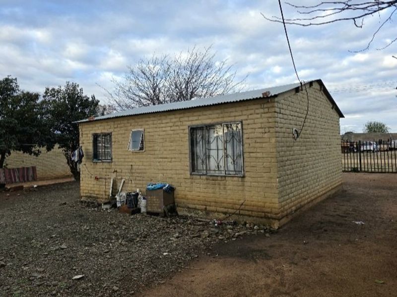 A detached single-story brick structure featuring a corrugated metal roof and security-barred windows, situated on an unpaved lot.