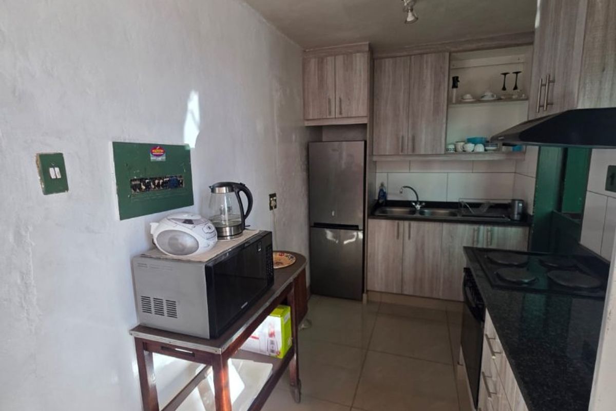 A functional galley-style kitchen featuring wood-look cabinetry, granite countertops, a built-in hob with extractor fan, and tiled flooring.