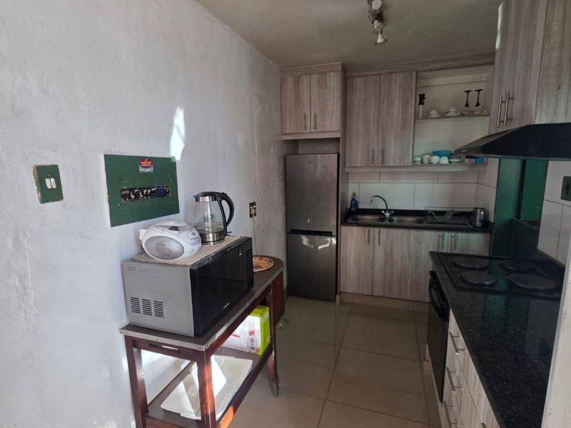 A functional galley-style kitchen featuring wood-look cabinetry, granite countertops, a built-in hob with extractor fan, and tiled flooring.