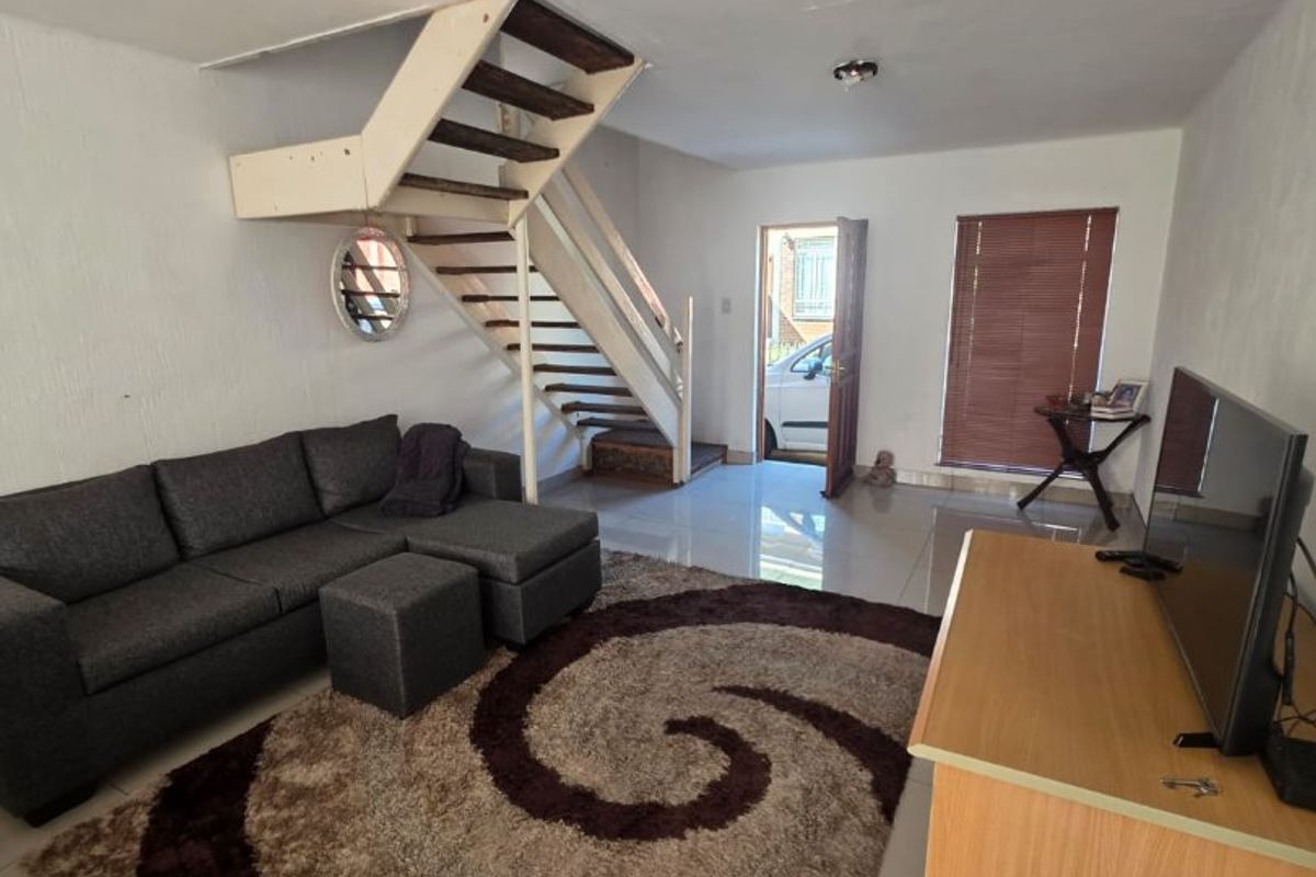 Open-plan living area featuring tiled flooring, a central staircase, and direct access to the exterior entrance.