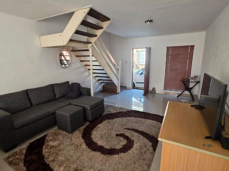 Open-plan living area featuring tiled flooring, a central staircase, and direct access to the exterior entrance.