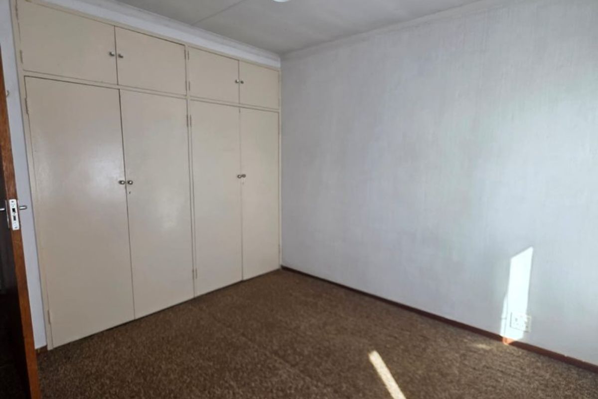 An empty bedroom featuring built-in cupboards, carpeted flooring, and a simple pendant light fixture, offering a blank canvas for renovation.