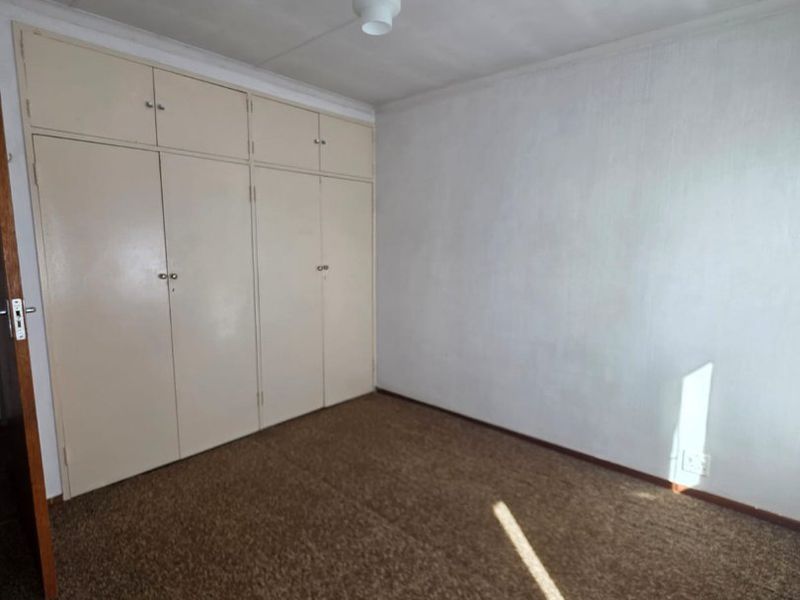 An empty bedroom featuring built-in cupboards, carpeted flooring, and a simple pendant light fixture, offering a blank canvas for renovation.