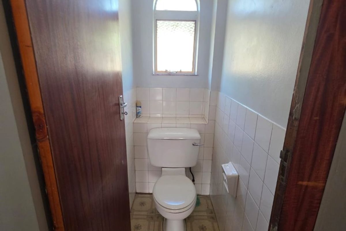 A compact guest toilet featuring an arched window, tiled splashback, and dated floor tiles, offering potential for a modern renovation.