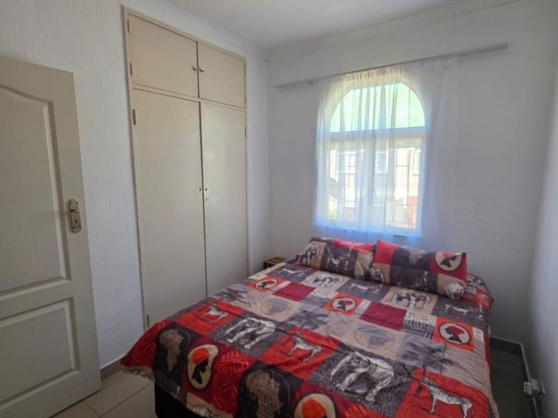 A bedroom featuring tiled flooring, built-in cupboards, and an arched window, providing a functional and well-lit living space.