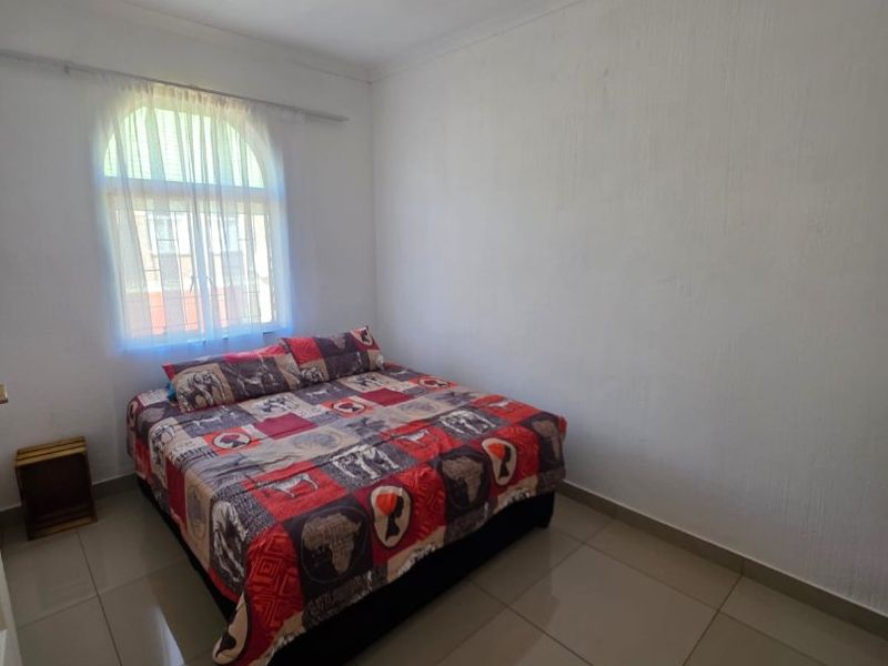 A simple bedroom featuring large format floor tiles, a distinctive arched window, and neutral wall finishes.