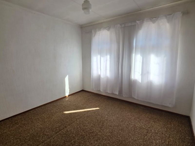 An empty bedroom featuring brown carpet flooring, white walls, and a central ceiling light fixture, offering a blank canvas for renovation.