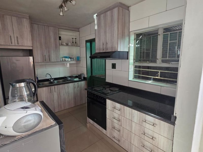 A functional kitchen featuring wood-look cabinetry, granite countertops, a built-in oven with hob, and tiled flooring, offering a practical workspace.