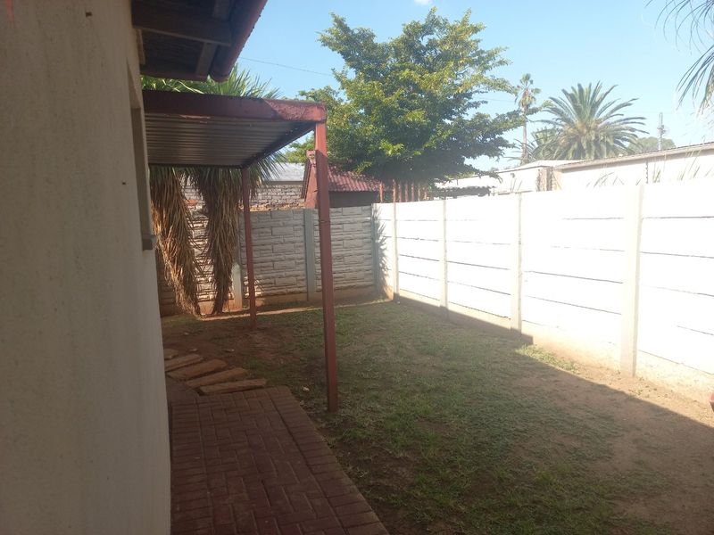 A private rear garden area featuring a paved walkway, a small covered patio space, and a secure precast concrete boundary wall.