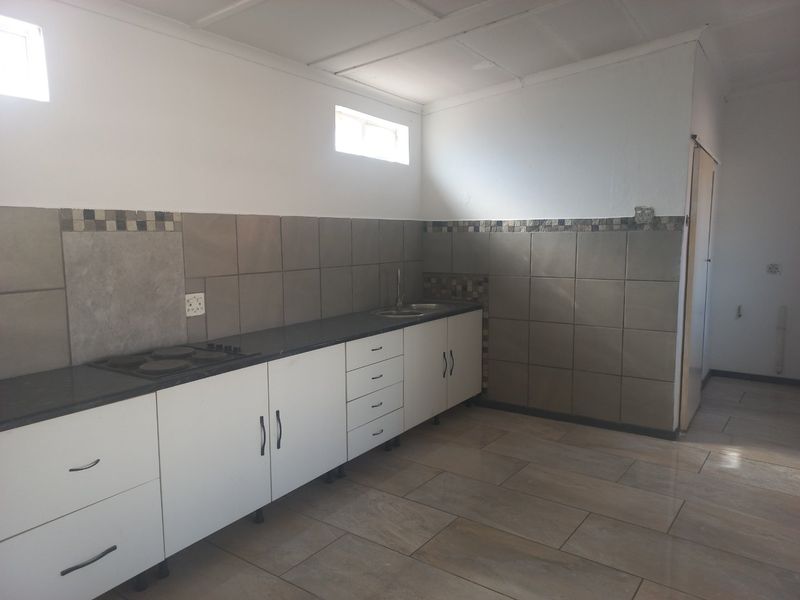 A functional kitchen featuring white cabinetry, a built-in hob, tiled backsplash, and tiled flooring, offering a clean and practical workspace.