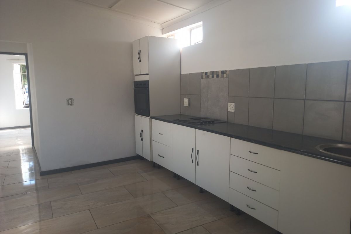 A clean, empty kitchen featuring white cabinetry, dark granite countertops, a built-in oven, hob, and neutral tiled flooring.
