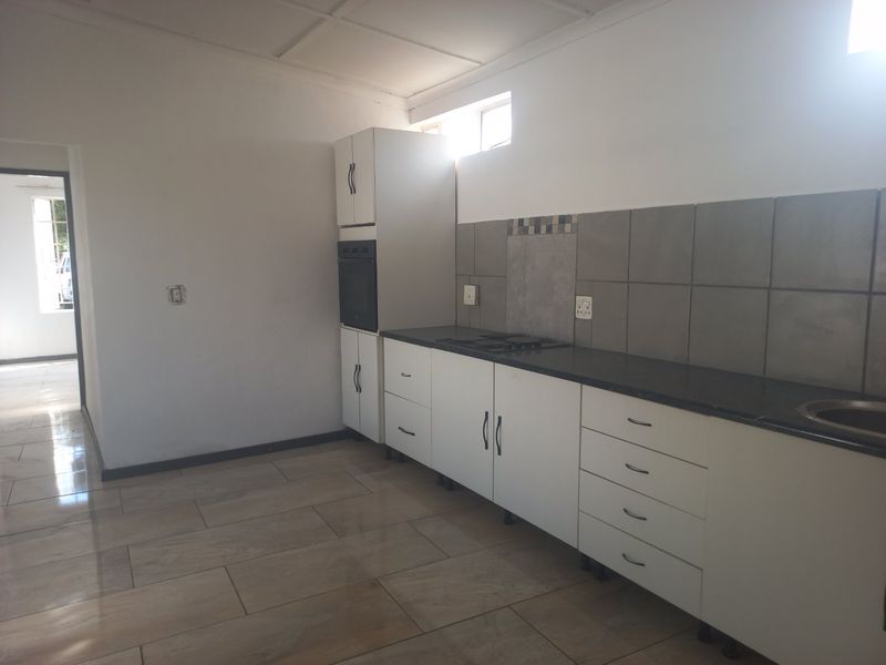 A clean, empty kitchen featuring white cabinetry, dark granite countertops, a built-in oven, hob, and neutral tiled flooring.