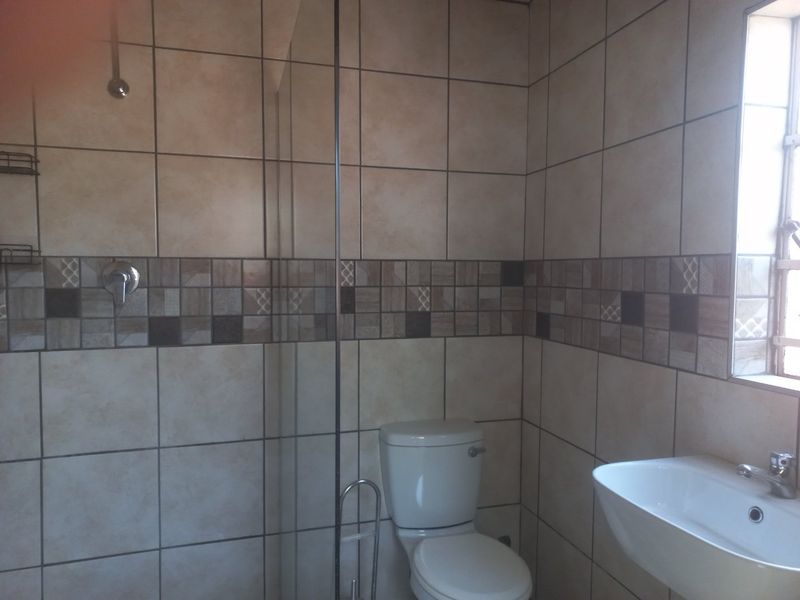 A functional bathroom featuring a glass-enclosed shower, a standard toilet, and a wall-mounted washbasin with tiled wall finishes.