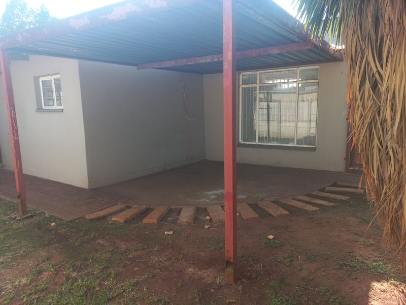 A covered outdoor patio area featuring a metal roof structure and paved flooring, requiring maintenance on the support posts.