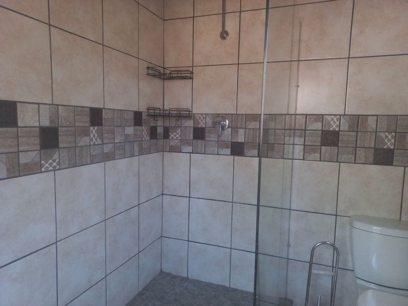 A functional bathroom featuring a walk-in shower with a glass screen, tiled walls with decorative accents, and a standard toilet.