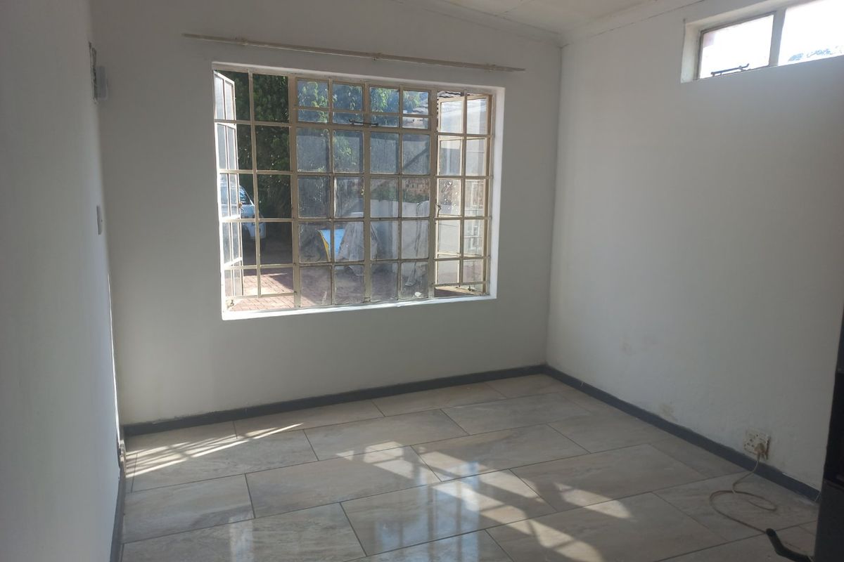 An empty bedroom featuring tiled flooring, steel-framed windows, and neutral walls, offering a blank canvas for personalization.