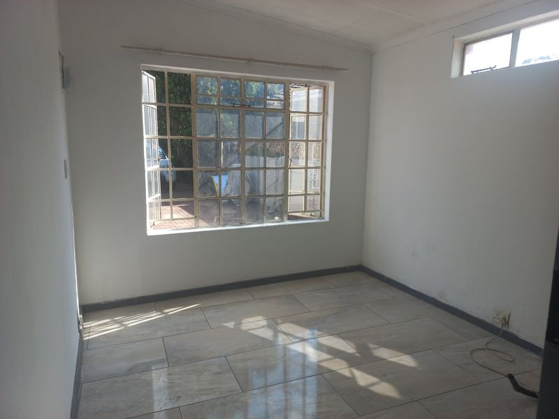 An empty bedroom featuring tiled flooring, steel-framed windows, and neutral walls, offering a blank canvas for personalization.
